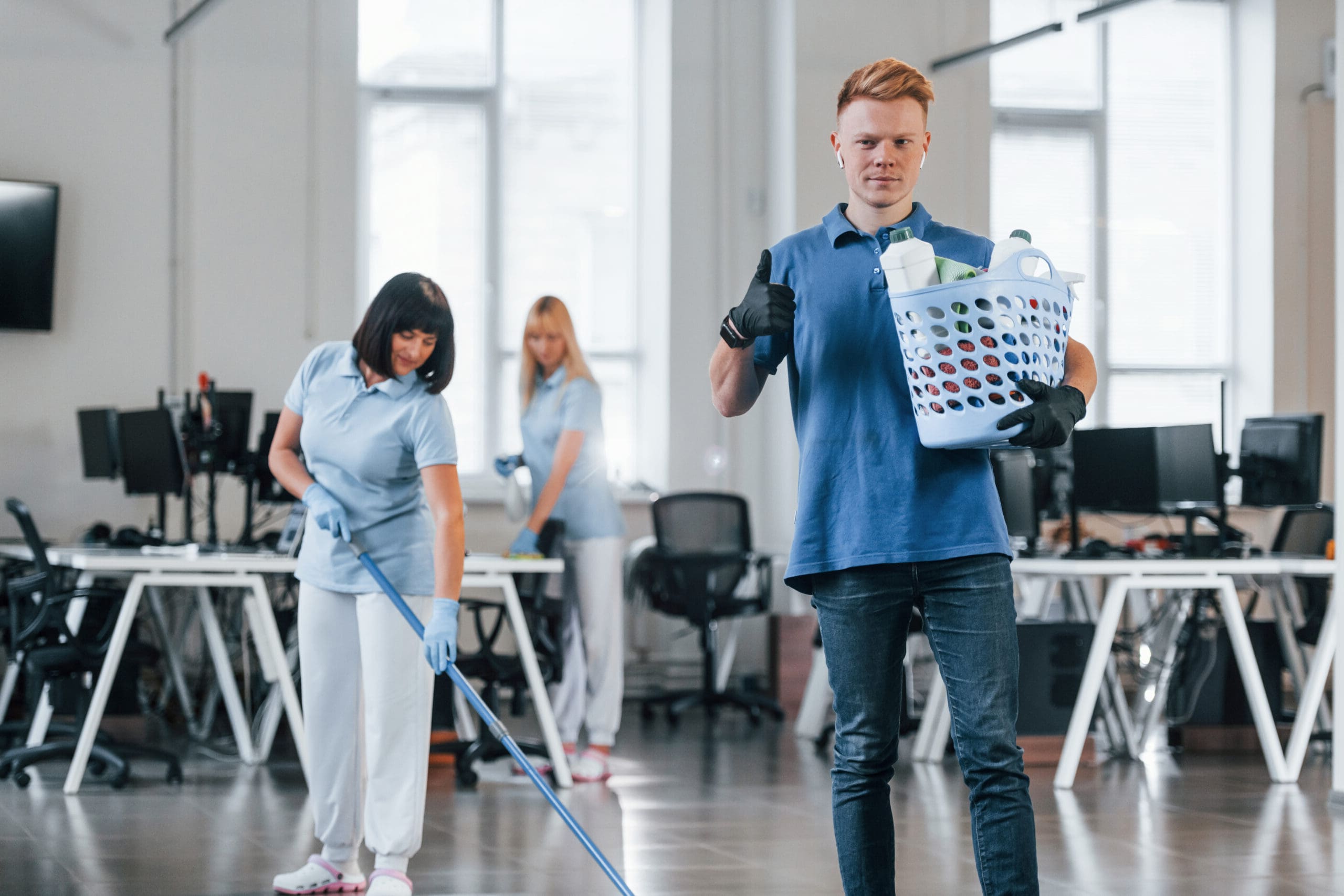 Man holds basket. Group of workers clean modern office together at daytime.